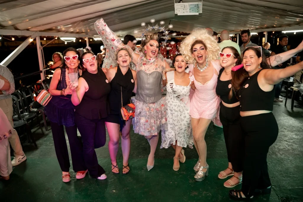 Amigas de una despedida celebrando con gafas de corazón junto a las drag queens en la fiesta en barco