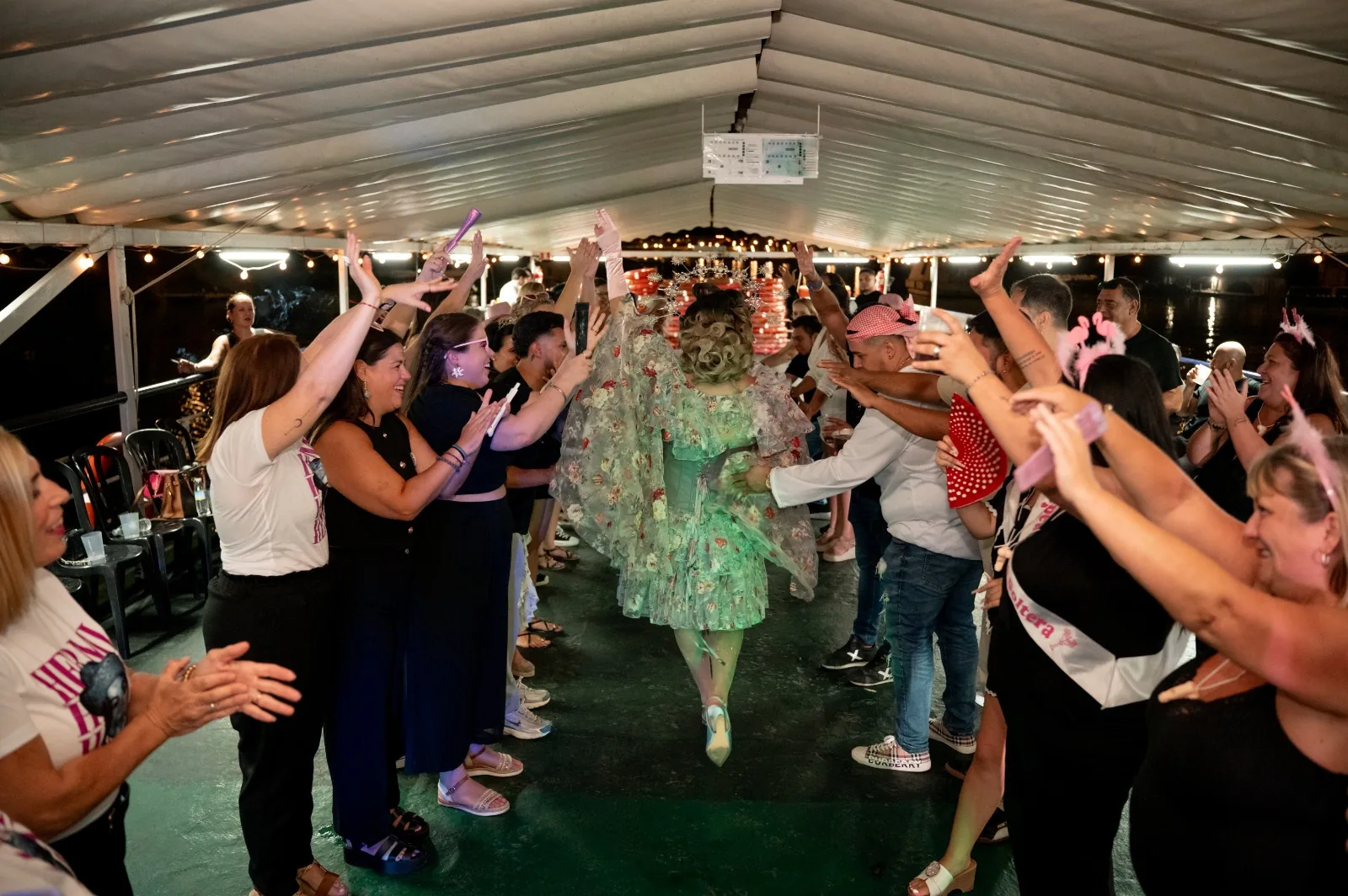 Drag queen con capa de flores avanzando entre invitados que la aplauden en la fiesta en barco por Sevilla