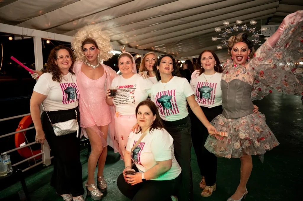 Grupo de despedida con camisetas personalizadas posando con las dos drag queens en el barco